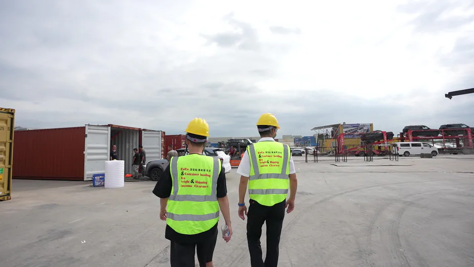 Two people wearing safety equipment walking through a container yard