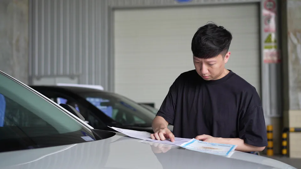 A person reviewing paperwork beside a vehicle